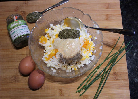 A bowl with minced eggs, mayonnaise and mustard with a jar of mustard and some eggs on the side