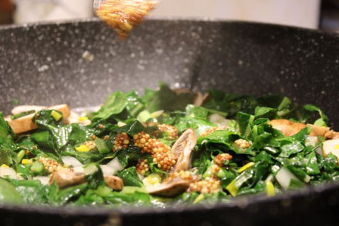 A pan with swiss chard. Mustard is falling into the pan