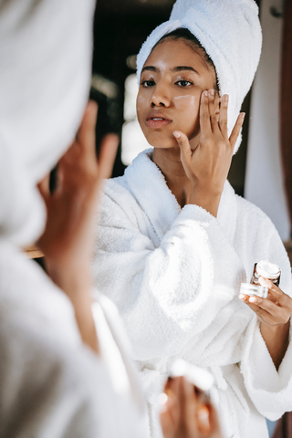 Woman in white robe and hair in white towel putting moisturiser on her face