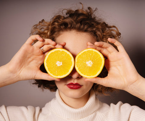 Woman covering her eyes with a cut orange