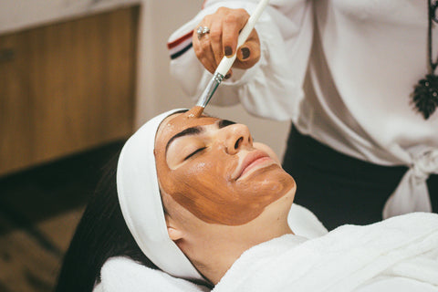 woman lying down getting a facial treatment with brown clay