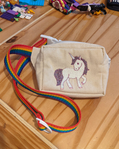 A smaller buff coloured bum bag with a cartoon unicorn embroidered on the front and rainbow webbing strap.