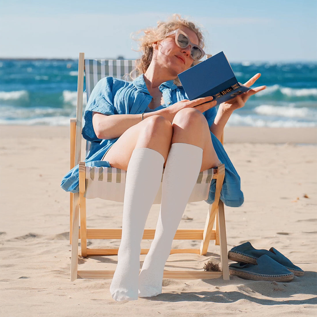 Sigvaris Summer Cotton Woman sitting on the beach, reading a book and wearing Sigvaris Essential Cotton compression socks