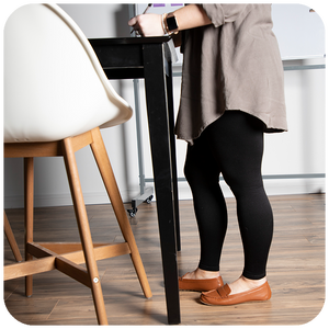 Woman standing at a draft desk, wearing Sigvaris Soft Silhouette compression leggings in Black
