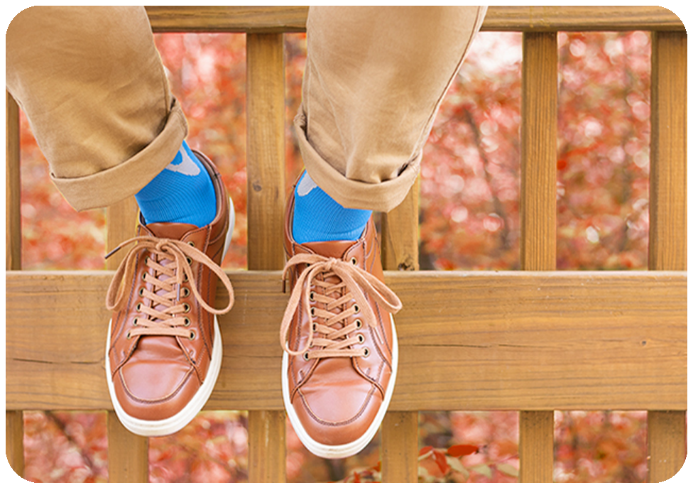 man's feet while sitting on a fence shows him wearing blue athletic compression socks