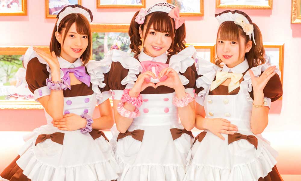 Three Japanese girls dressed in a maid style outfit in a Japan Maid Cafe. They are wearing maid skirts and bow ties.