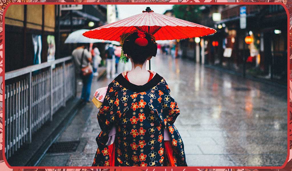 A Japanese women wearing a traditional geisha kimono in Tokyo street. She is walking in the street with an umbrella. Her hair is embellished with a Kanzashi comb