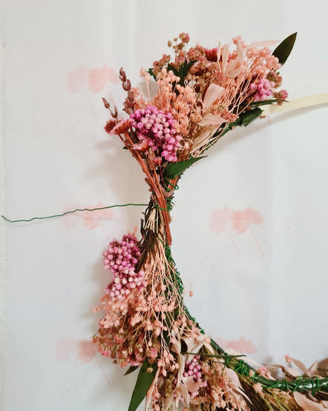 Bovenaanzicht van een zelfgemaakte roze bloemenkroon van droogbloemen waarbij de laatste centimeters nog moeten worden opgevuld.