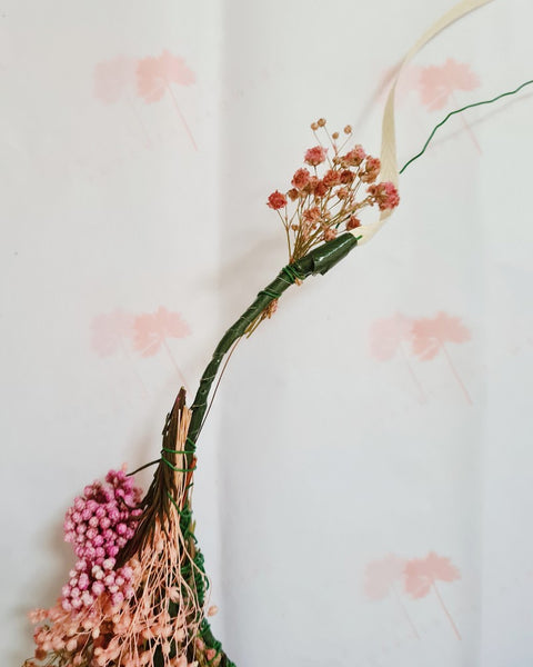 Een zelfgemaakte bloemenkroon van droogbloemen die bijna klaar is met roos gipskruid, eucalyptus en rijstbloemen