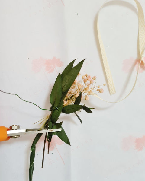 Een knipschaar knipt de stelen van droogbloemen die op een bloemenkroon gebonden worden kort