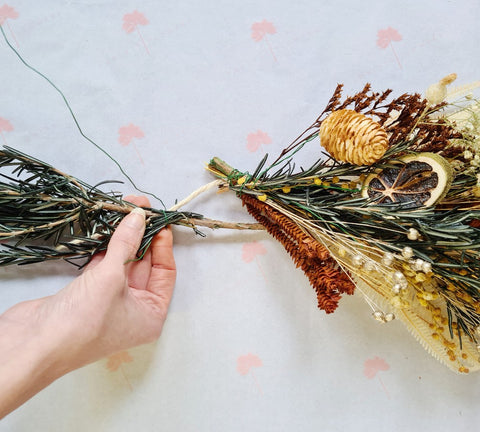 Gepreserveerde rozemarijn aan het touw binden met ijzerdraad voor een DIY kerstguirlande