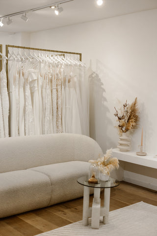 Showroom gevuld met gouden kledingrek vol moderne bruidsjurken en beige ronde zetel