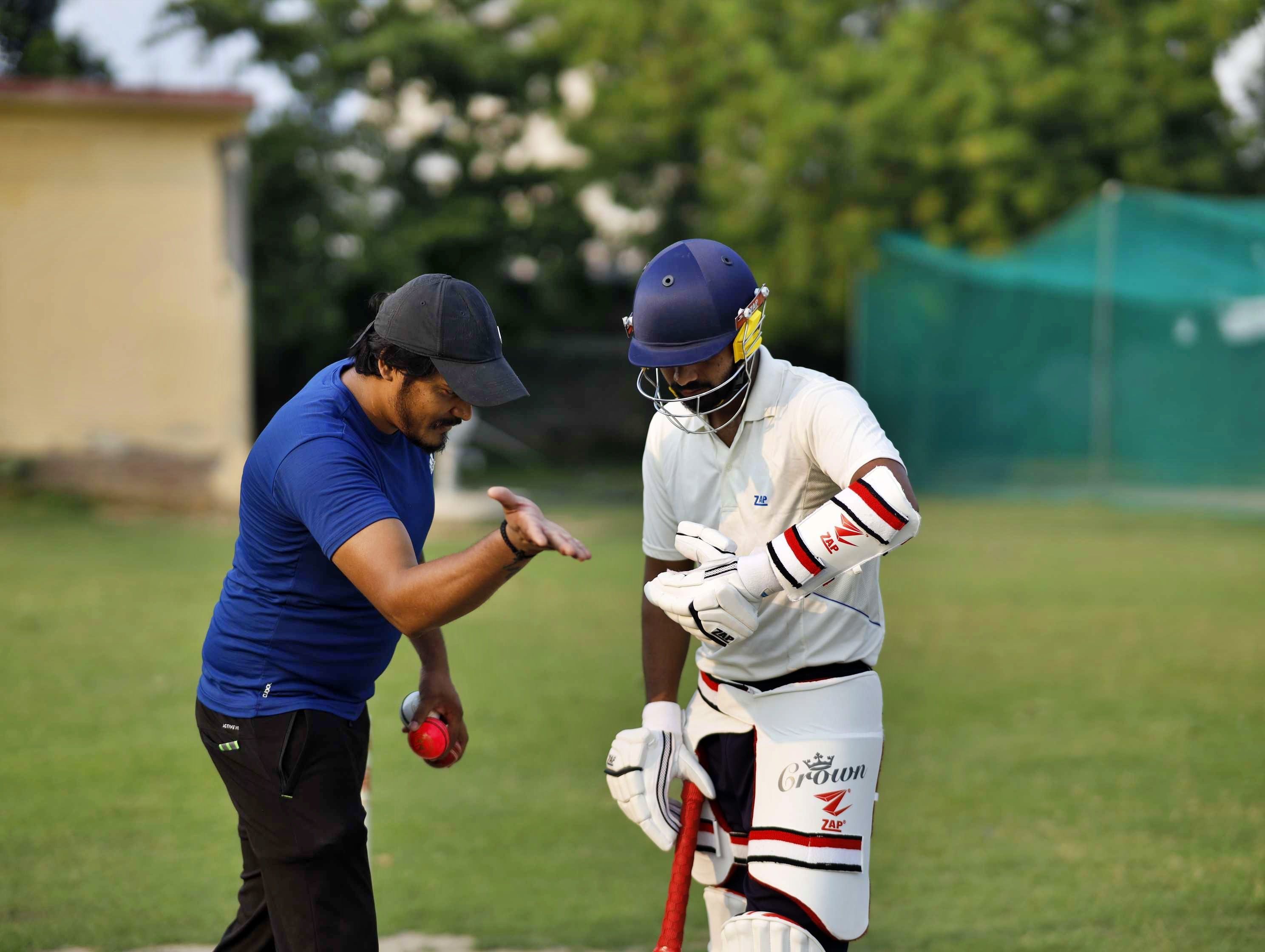 A cricket coaching teaching an academy player how to play a cover drive