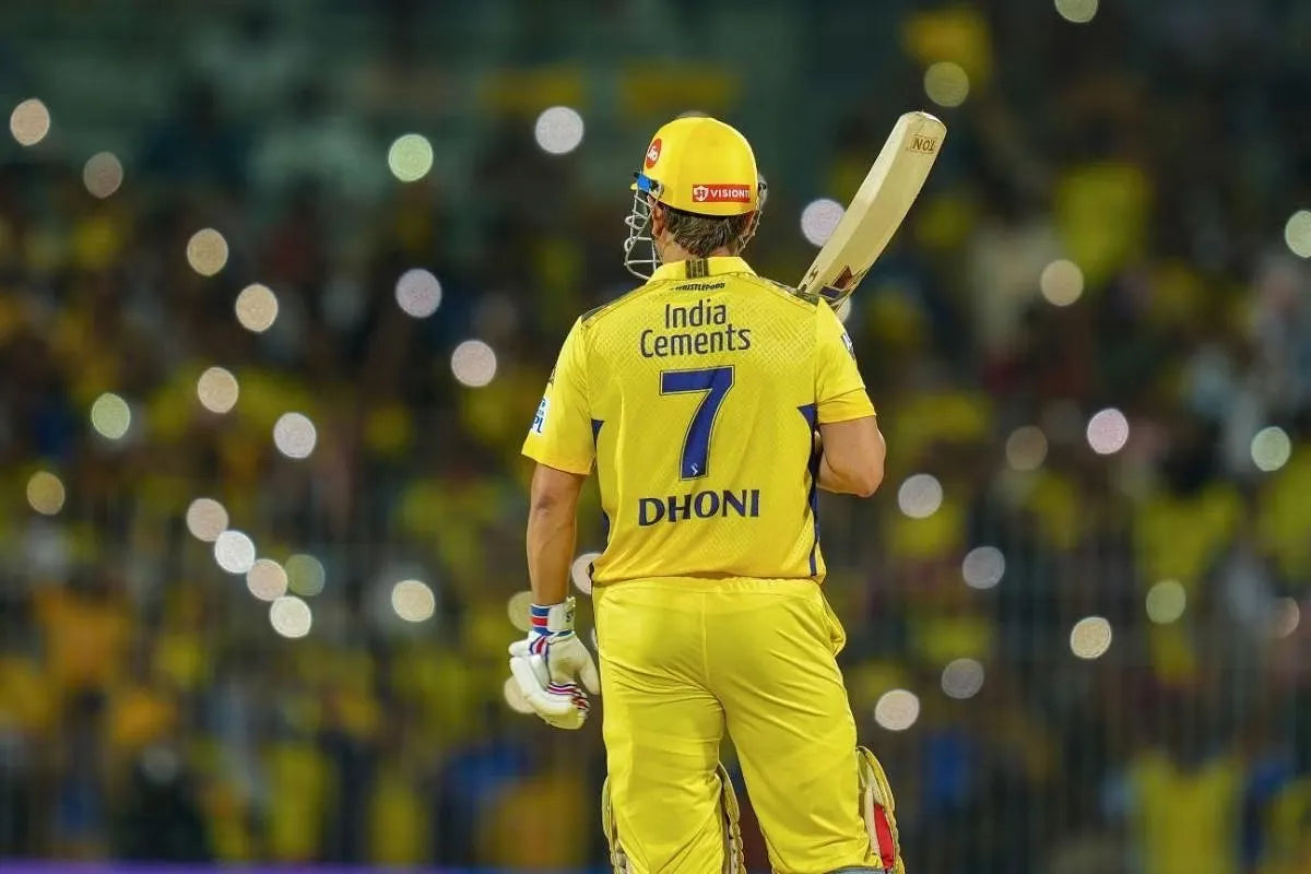 A picture of Dhoni standing with his bat in his hand and a beautiful backdrop of people with their phone cameras on