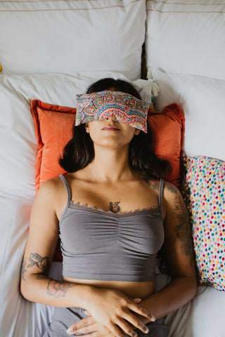 Woman Laying On Bed With Lavender Eye Pillow Over Her Eyes 