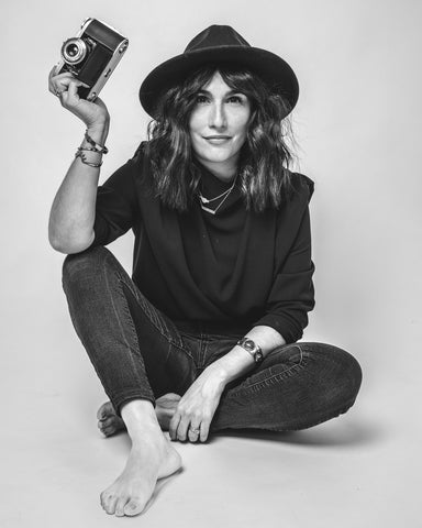 Woman seated in photo studio with hat and camera in black and white