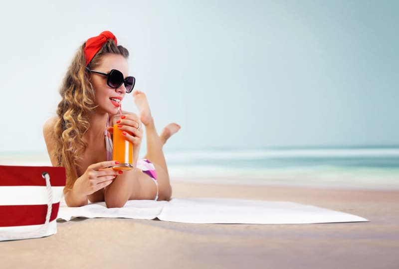 Pin-up sur la plage avec un nœud rouge dans les cheveux, ainsi qu'un verre de jus à la main