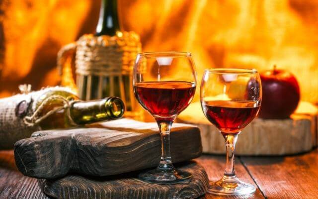 Feiner roter Dessertwein in zwei Gläsern auf einem gedeckten Tisch mit Feuer im Hintergrund