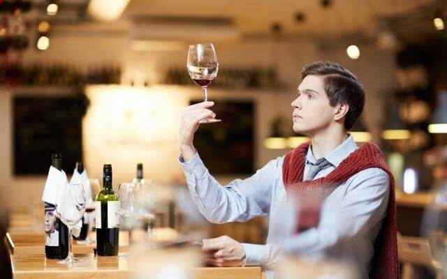 Mann hält Weinglas in die Höhe und schaut sich die Farbe des Weins genau an