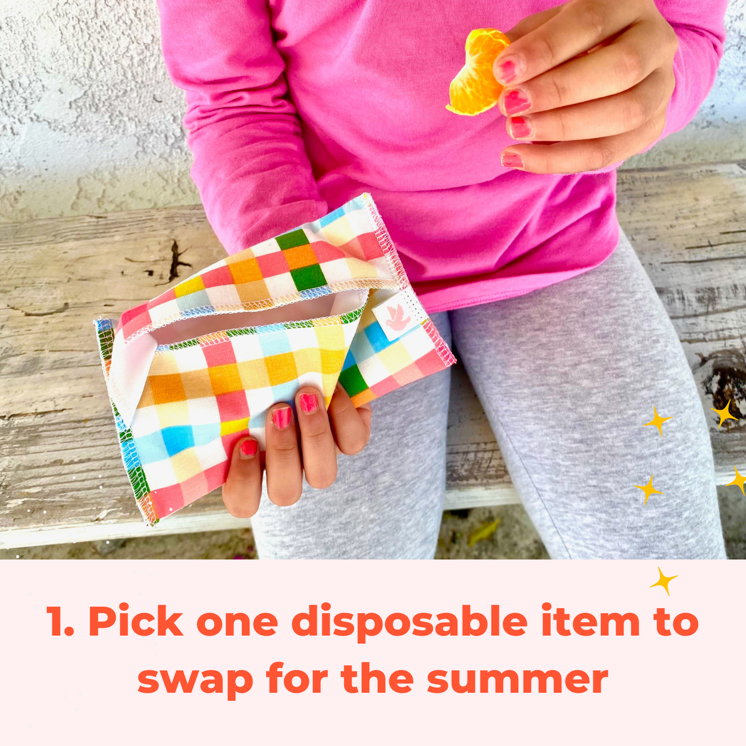 child's hand holding a reusable plaid snack bag in one hand an an orange slice in the other