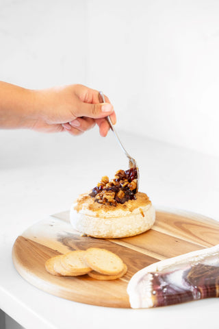 putting mixture on top of baked brie cheese on cheese board