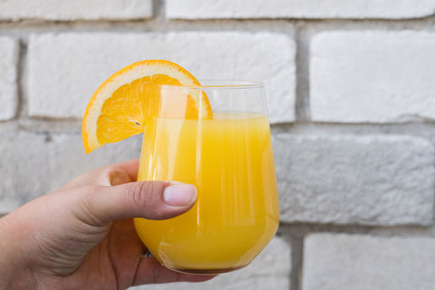mimosa being held in hand with an orange slice on the glass