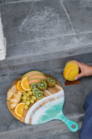 resin accented paddle shaped cheese board served with fruit and a mimosa