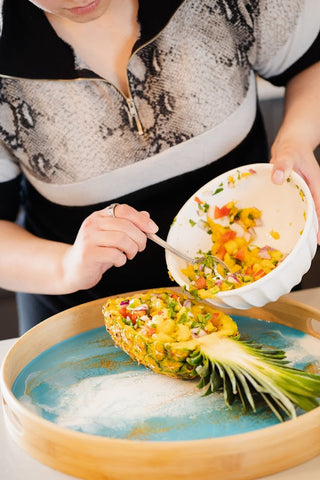 adding the pineapple salsa mixture into empty inside half of pineapple and placing of bamboo serving tray