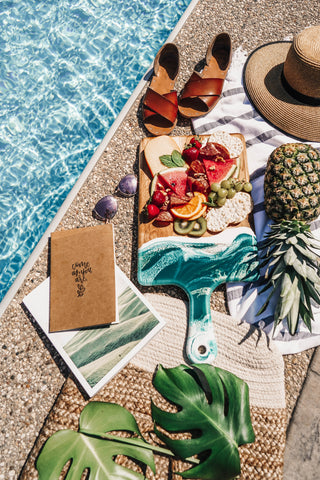 Summer by the pool on a sunny day with a cheese board served with meat, cheese, and fresh fruit