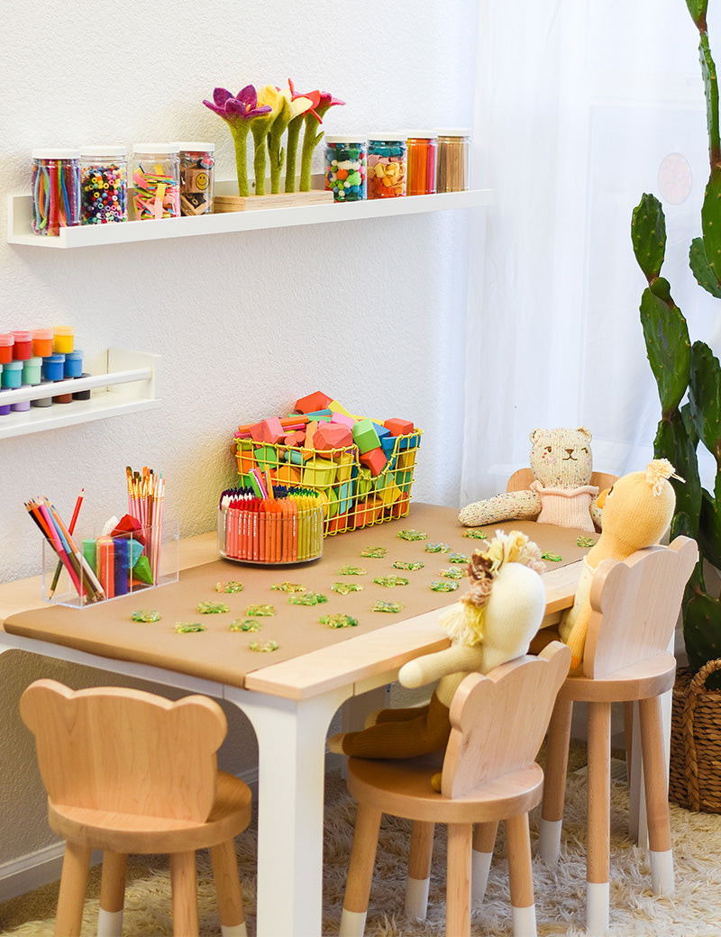 Three little dolls set on wood animal-shaped chairs next to the craft kids table. 