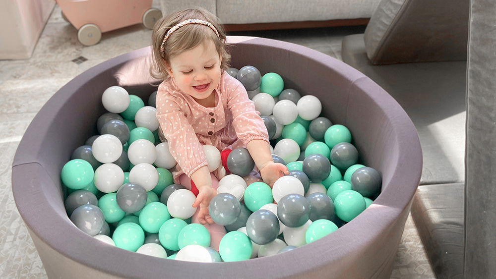 Little girl playing with the balls while sitting in the ball pit.