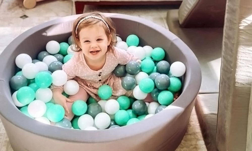 Little girl looking up and smiling from her ball pit.