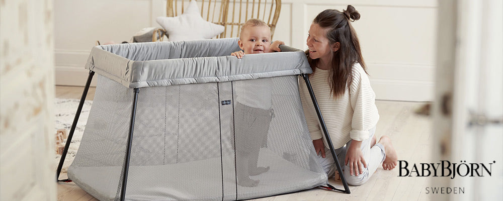 mom smiling at child standing in babybjorn travel crib light