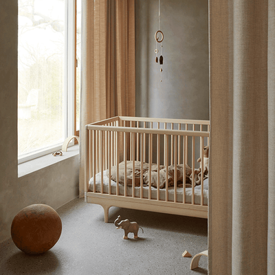 the half view of oiled ash caravan crib in the bedroom with mattress and toys on the crib and floor -- Lifestyle