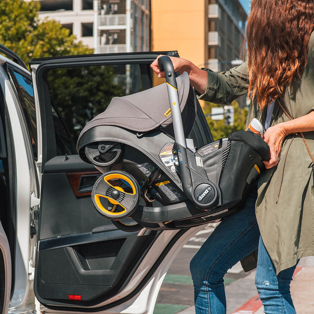 Women putting Doona Infant Car Seat and Stroller in Grey Hound in back seat of the car -- Color_Greyhound