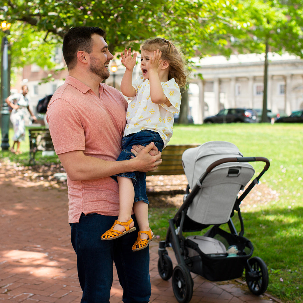 Man holding the child and standing beside the vista v2 stroller -- Color_Anthony