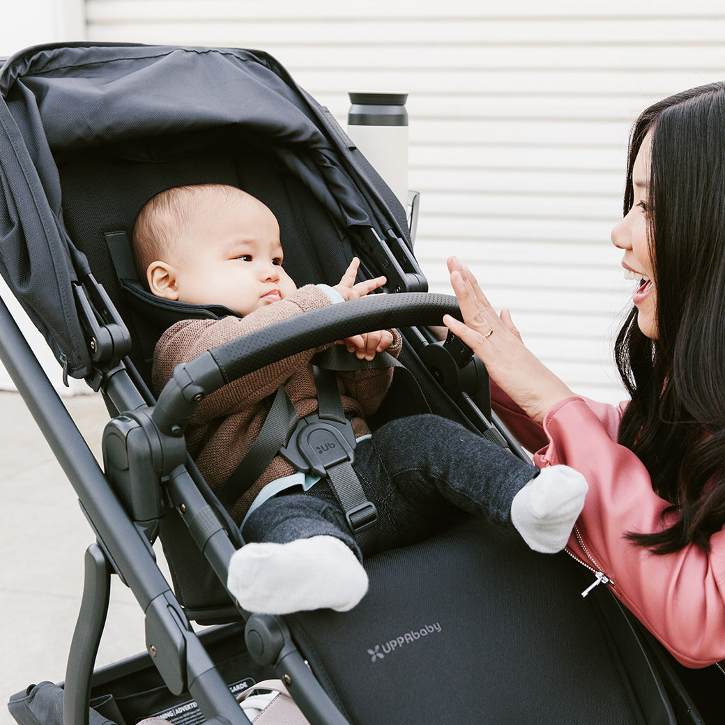 woman kneeling beside the vista v2 stroller in Jake while playing with child in stroller -- Color_Jake