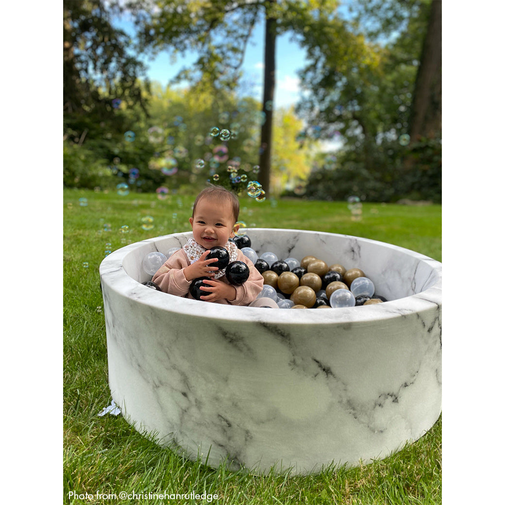 Baby sitting in marble ball pit holding balls and laughing -- Lifestyle