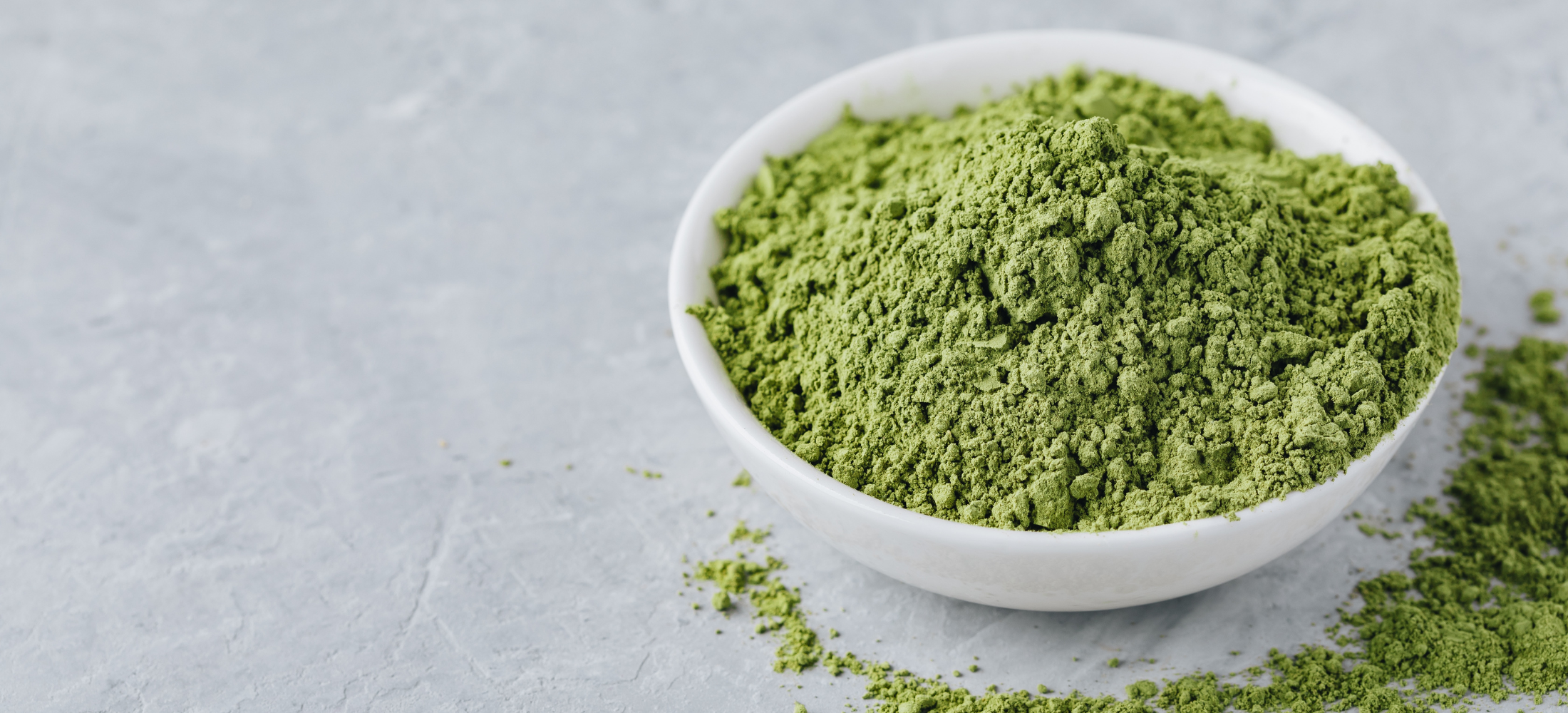 green matcha powder in a white round bowl on grey countertop. 