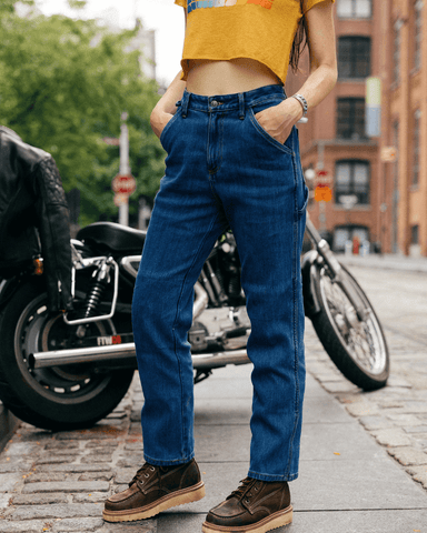 An image of a woman standing on a brick road in Brooklyn, NY wearing the Utopia relaxed fit motorcycle jeans for women