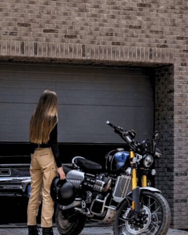 An image of a brunette woman faced away from the camera holding a helmet and wearing the women's Mila Cargo motorcycle rider pants