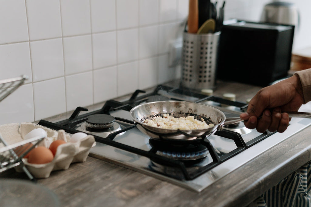 person holding stainless steel cooking pan on gas cooktop