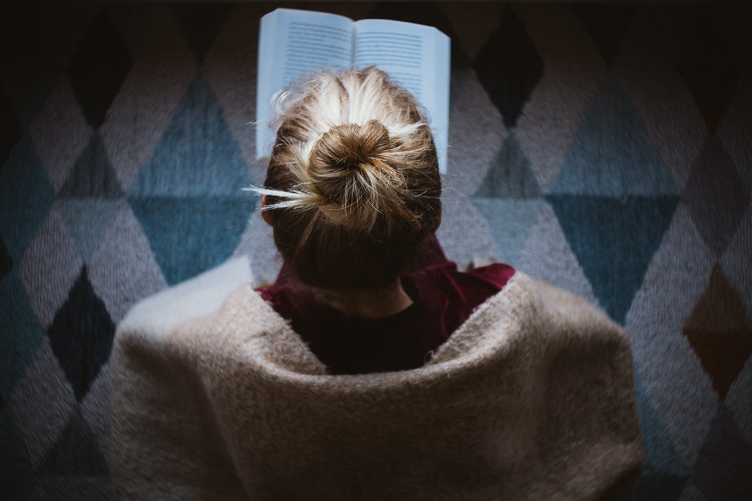 woman with blonde hair tied in a bun reading a book wrapped in a brown sweater looking over her shoulder geometric carpet burnside 35 comparison