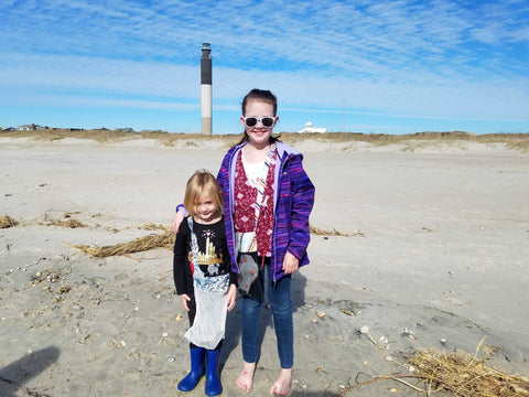 Two girls on sandy beach with light house in the background.