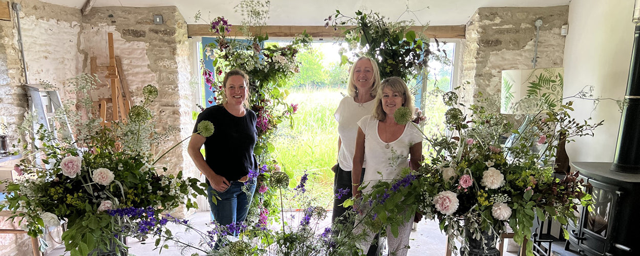 Photo shows three participants at the Eco Flowers Retreat at Common Farm Flowers with large arrangements they've made on Day 3 of the workshop. The arrangements are full of summer flowers grown sustainably on the Somerset flower farm.