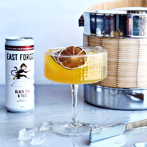 Can of East Forged Black tea near a glass of cocktail and ice bucket