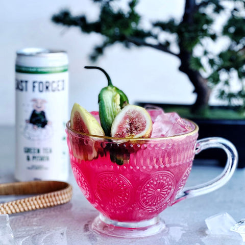 can of east forged tea next to a bright pink cocktail and bonsai tree