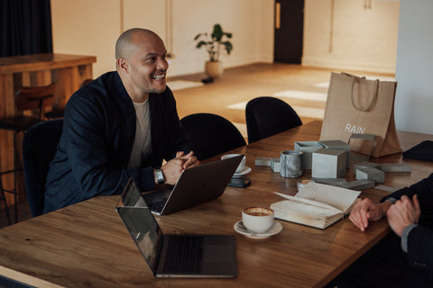 Harry Jameson sitting at a table with two laptops on the table and RAIN products while having a meeting. 