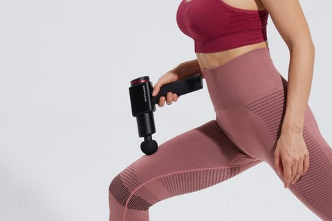 Woman using a massage gun on her thigh while doing a lunge