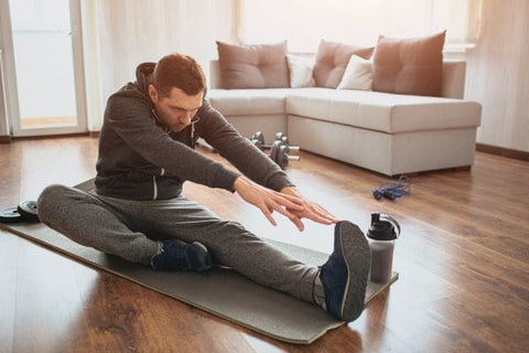 Man sitting on a yoga mat and reaching for his toe